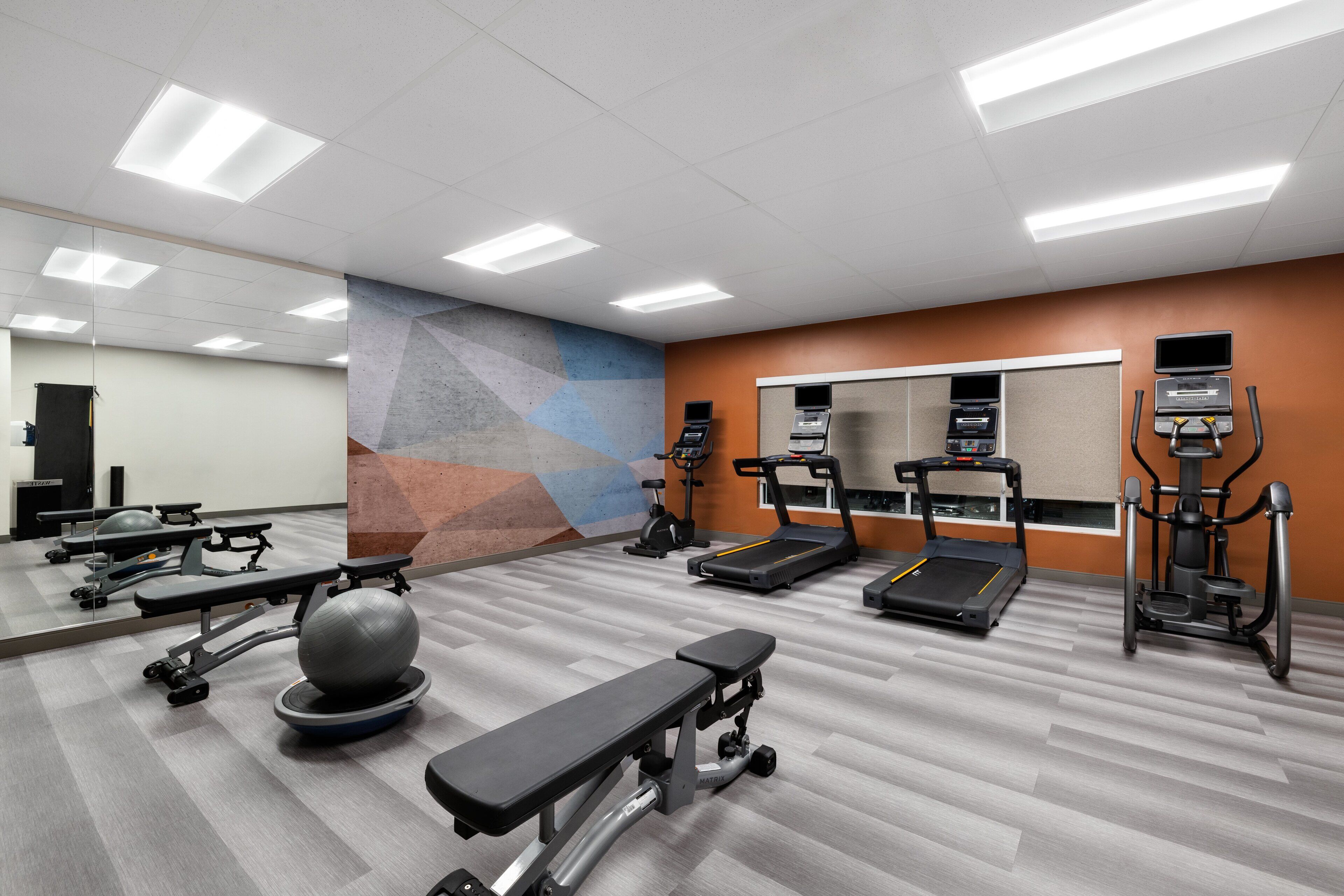 Une salle de sport équipée de matériel d’exercice, dotée d’un mur miroir et d’un motif géométrique sur un autre mur.