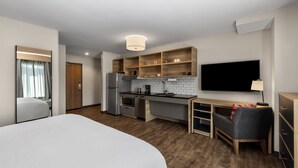 A modern hotel room with a large bed, a kitchenette, a flat-screen TV, and a small seating area.