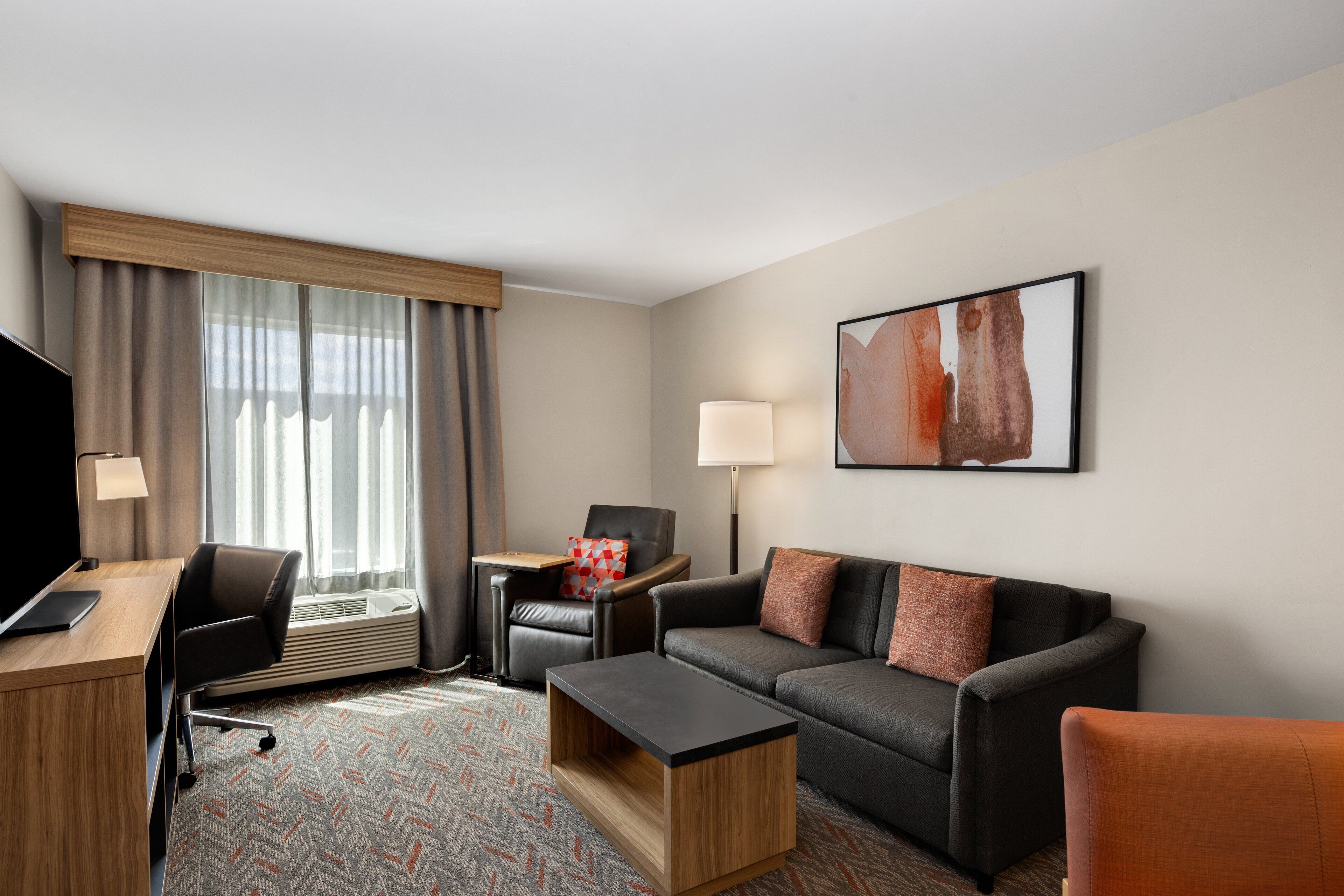 A hotel room with a desk, a black leather chair, a sofa, a coffee table, and a TV.