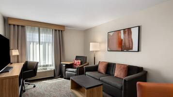 A hotel room with a desk, a black leather chair, a sofa, a coffee table, and a TV.