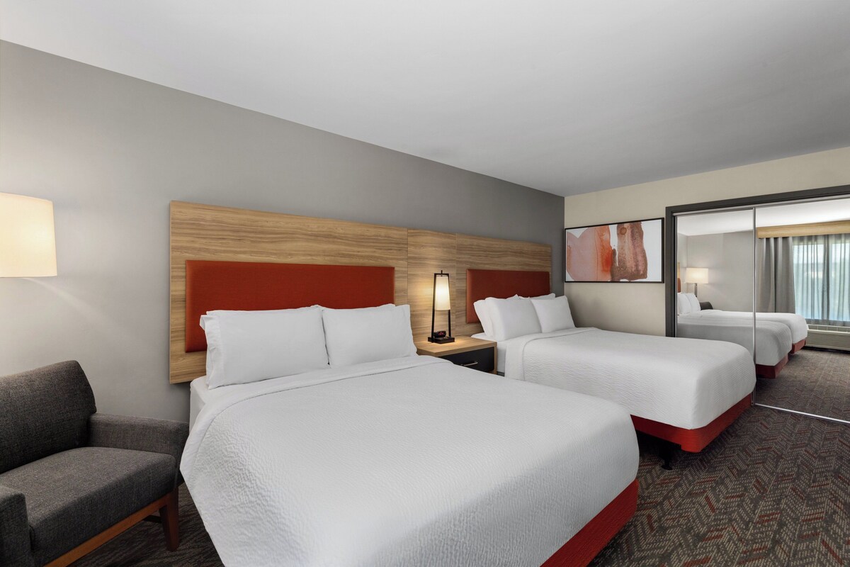 A hotel room with two beds, a sofa, a nightstand, and a mirror.
