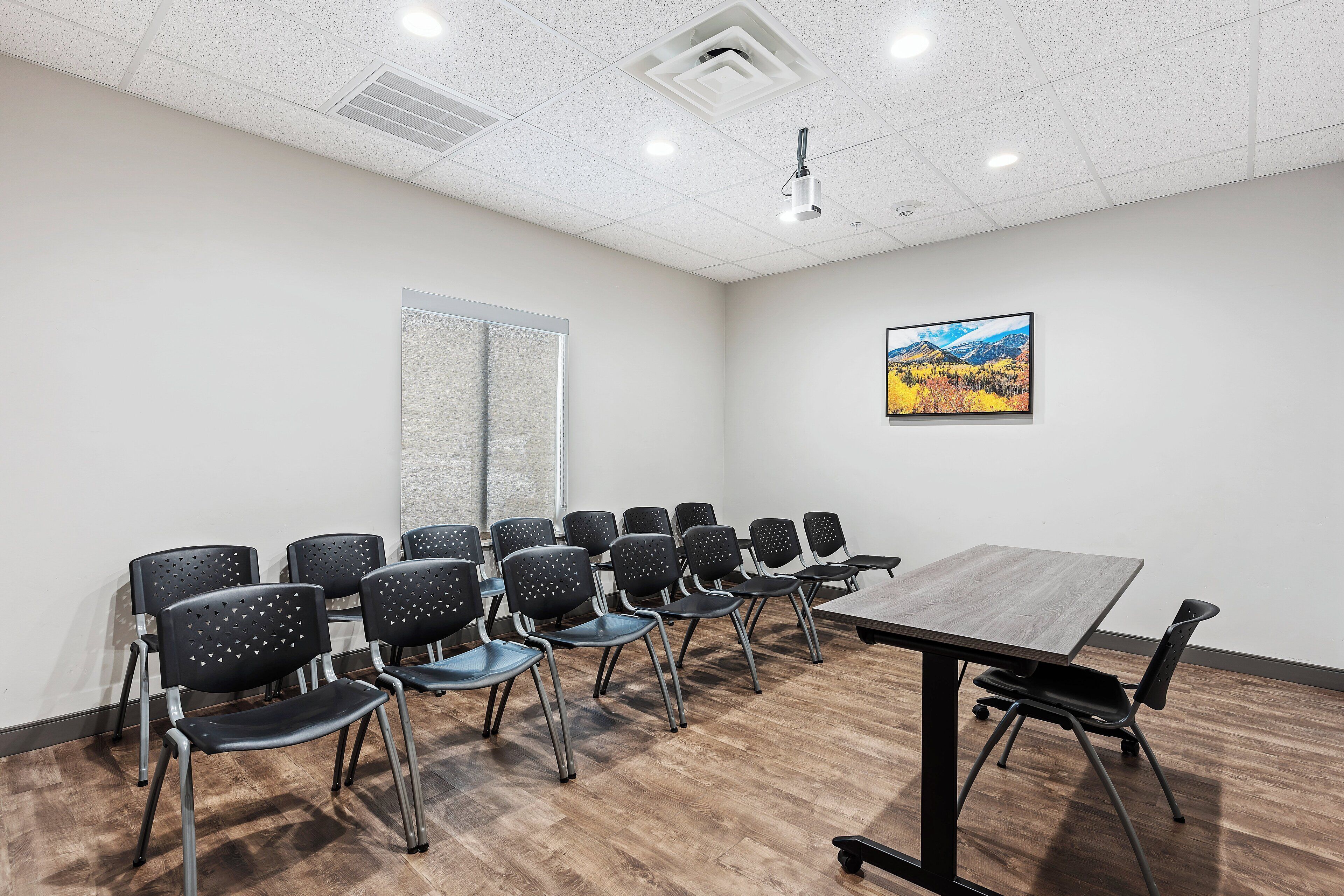 Un salón de conferencias con una larga mesa y numerosas sillas, un ventanal grande y un cuadro en la pared.