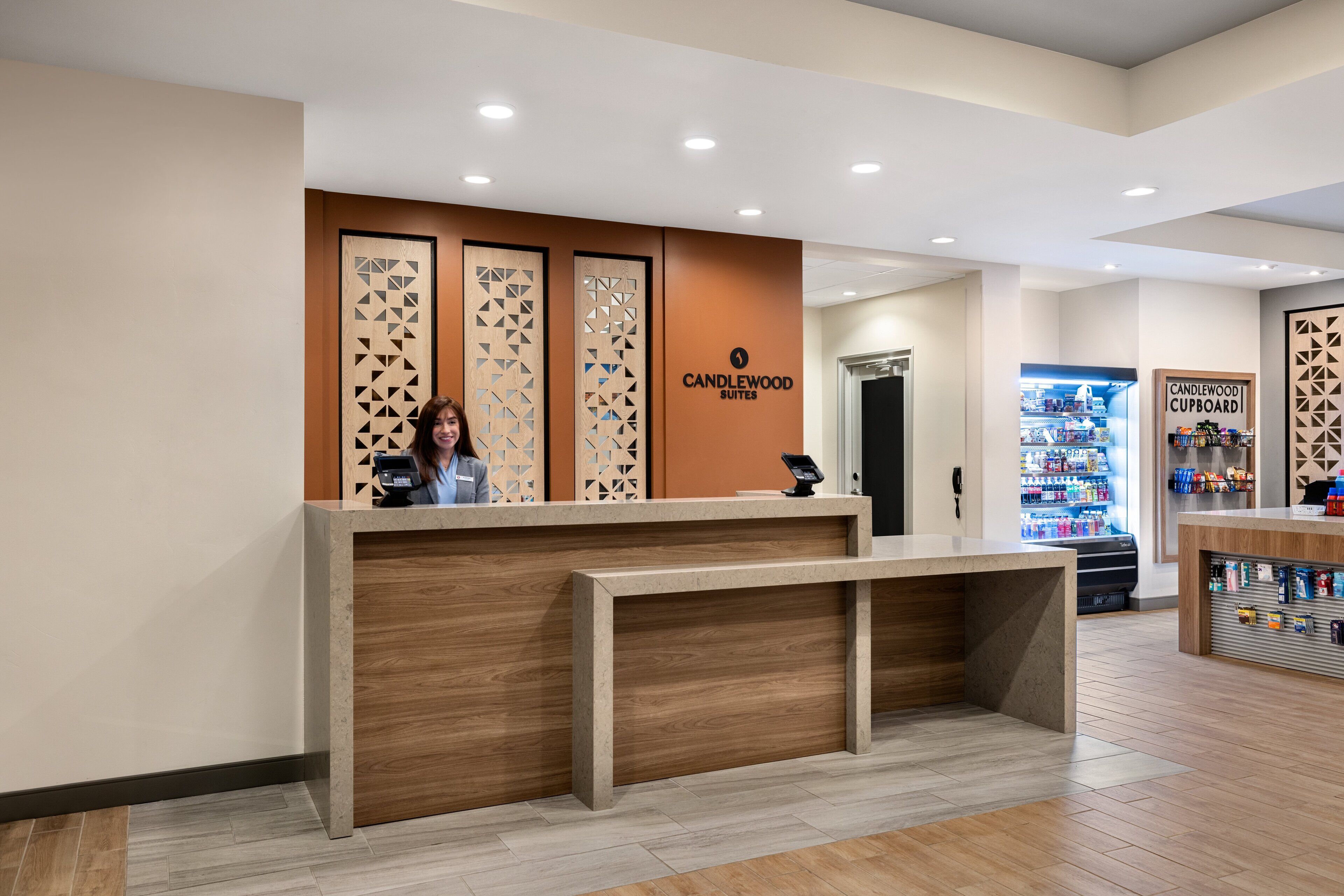 Un mostrador de recepción de diseño moderno, un letrero de Candlewood Suites y un refrigerador en el fondo.