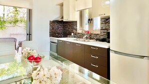 A modern kitchen with a stainless steel refrigerator, dark brown cabinets, a glass countertop, and a backsplash with mosaic tiles. - Luxury Villa San George with private pool (Perigiali)