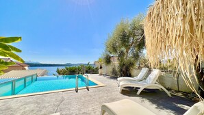 A pool area with lounge chairs, a clear view of the sea, and a mountain in the distance. - Luxury Villa San George with private pool (Perigiali)