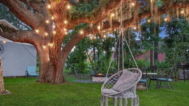Un albero con luci a stringa, una poltrona a dondolo e mobili da esterno sotto un grande albero.