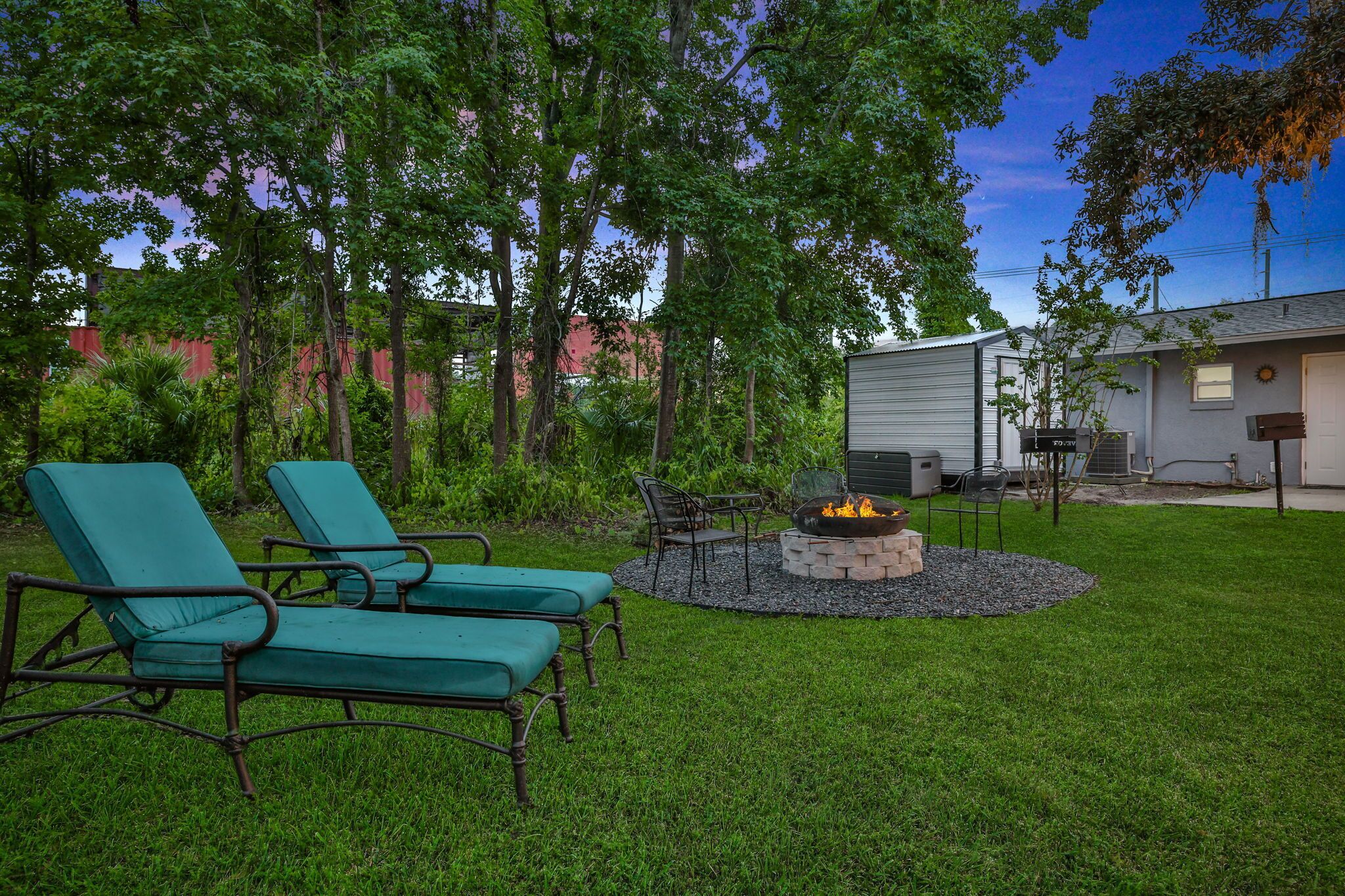 A backyard with two green lounge chairs, a fire pit, and a patio table.
