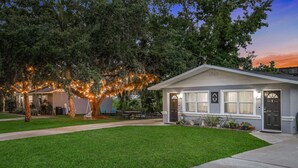 Una casa a un piano con un prato curato, un portico con mobili da esterno e un albero decorato con luci.