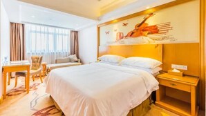 A hotel room with a large bed, a desk, a chair, and a window with curtains. - Vienna International Hotel (Foshan)