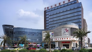 A modern hotel with a prominent sign, a curved glass facade, and a parking area with several cars. - Vienna International Hotel (Foshan)