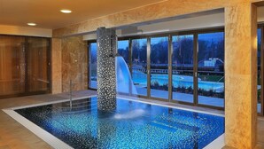 Una piscina interior con pared de mosaicos, ventanas amplias y vista a un paisaje nevado.