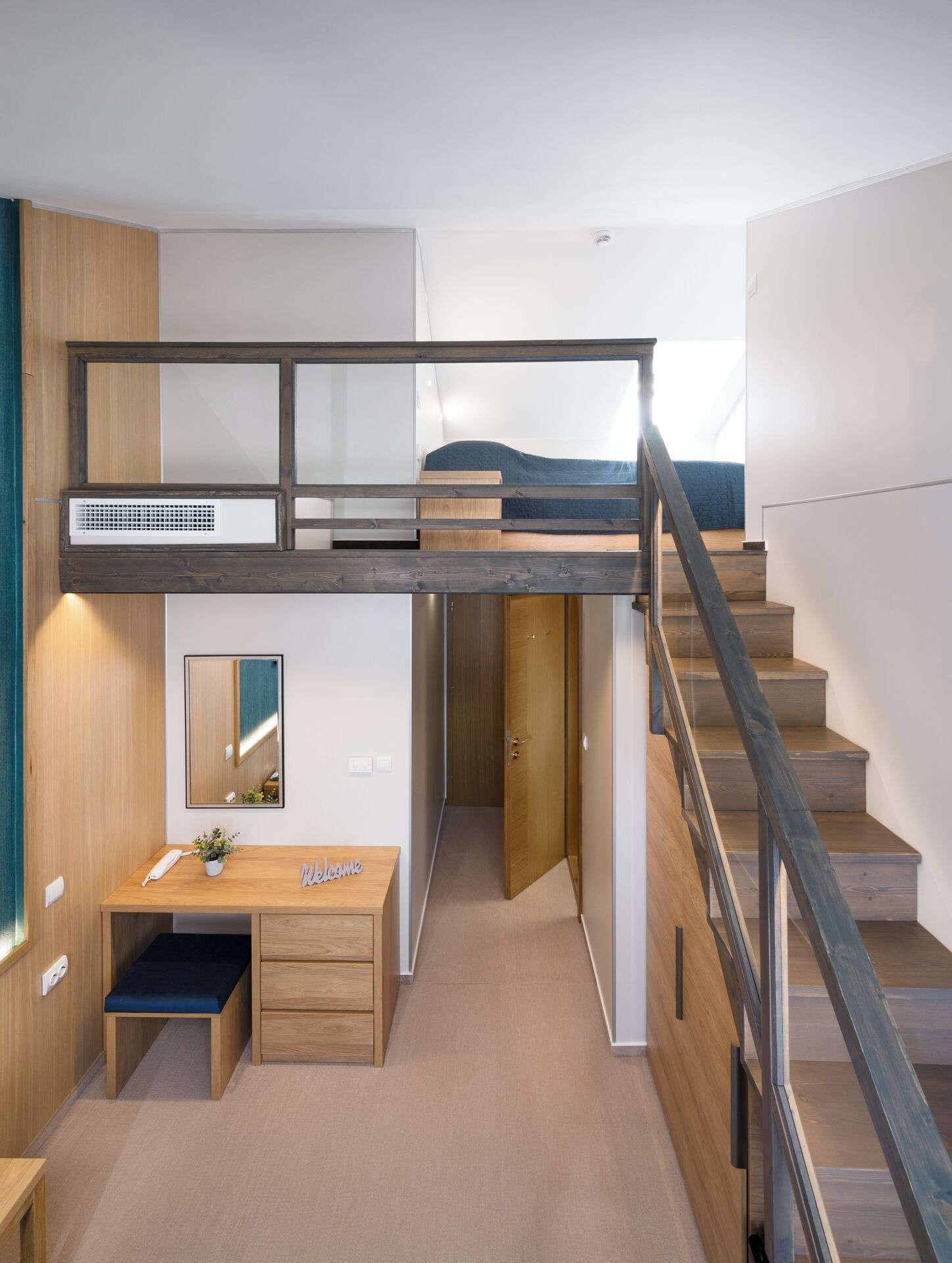 A modern bedroom with a bunk bed, a desk with a chair, a mirror, and a staircase.