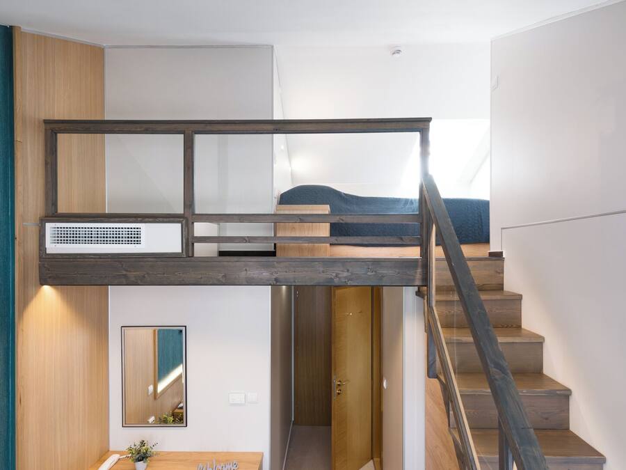 A modern bedroom with a bunk bed, a desk with a chair, a mirror, and a staircase.