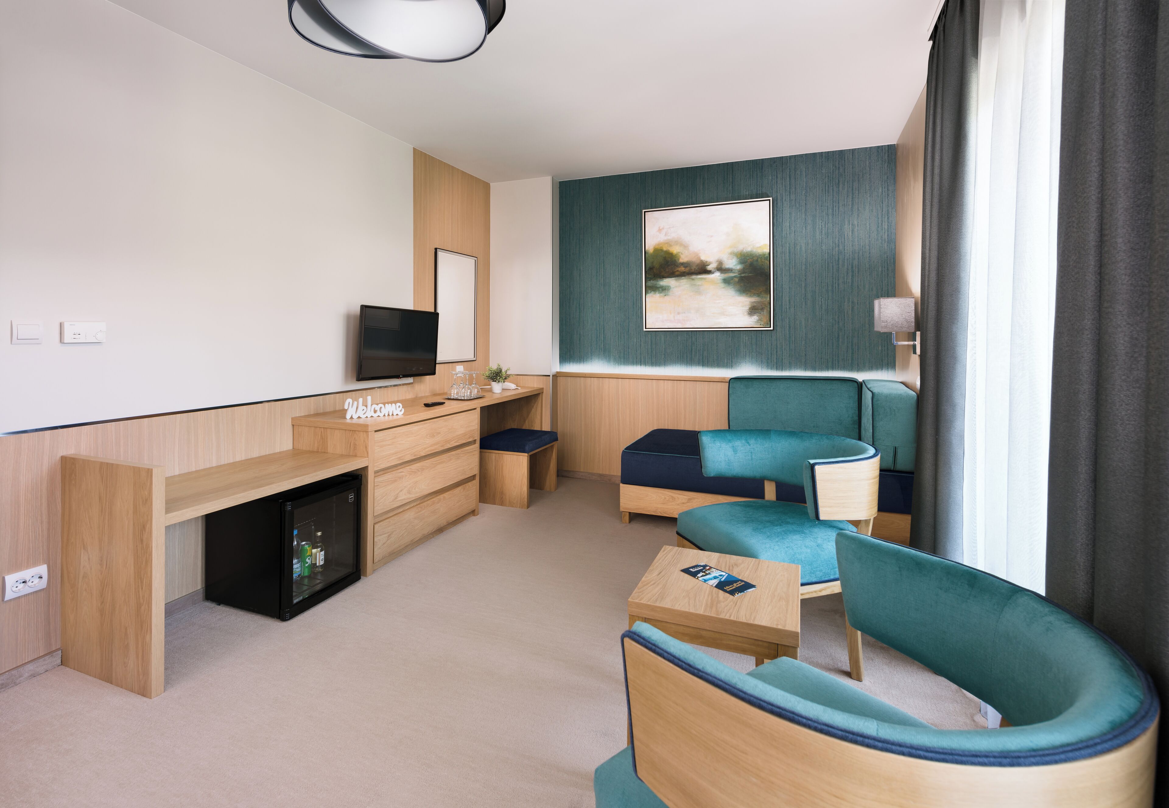 Una habitación de hotel moderna con un escritorio de madera, un televisor, un sofá y un cuadro en la pared.