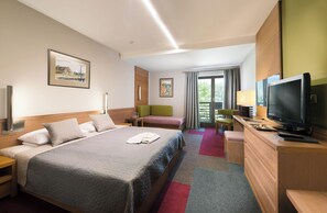 Une chambre d’hôtel avec un grand lit, un bureau avec une télévision, une chaise, un canapé et une fenêtre avec des rideaux.