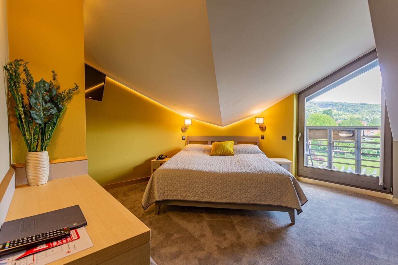Un dormitorio con una cama grande, lámparas de noche, un escritorio con un control remoto y vistas a un balcón.