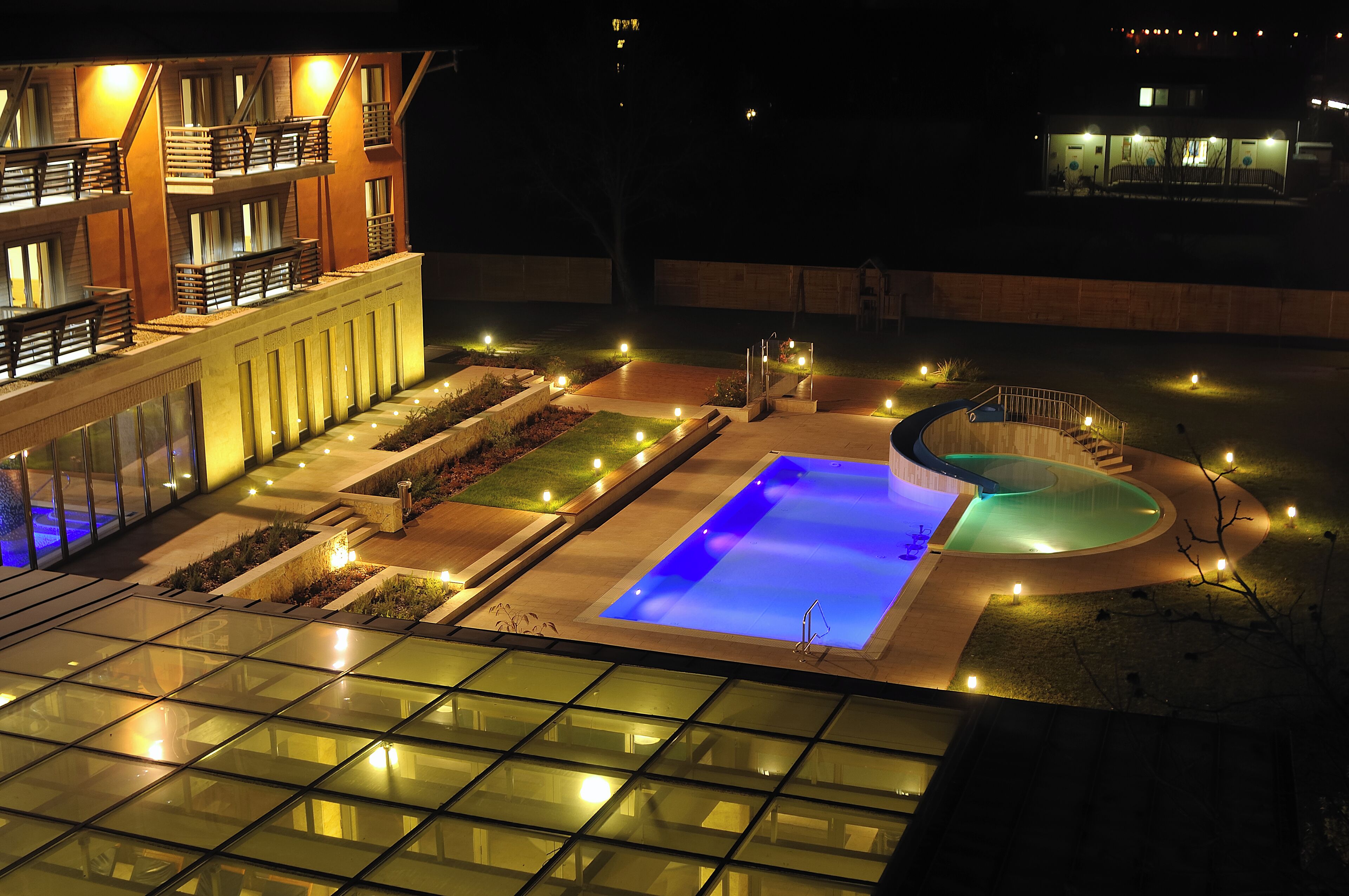 Un hotel moderno con piscina, iluminación exterior y fachada de vidrio.