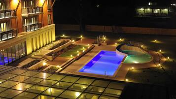 Un hotel moderno con piscina, iluminación exterior y fachada de vidrio.
