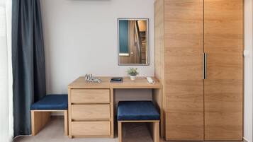 A modern room with a wooden desk, a bench, a wardrobe, a TV, and a mirror.