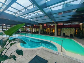 Une piscine intérieure dotée d’un toit en verre transparent, de chaises longues et d’un sol carrelé.