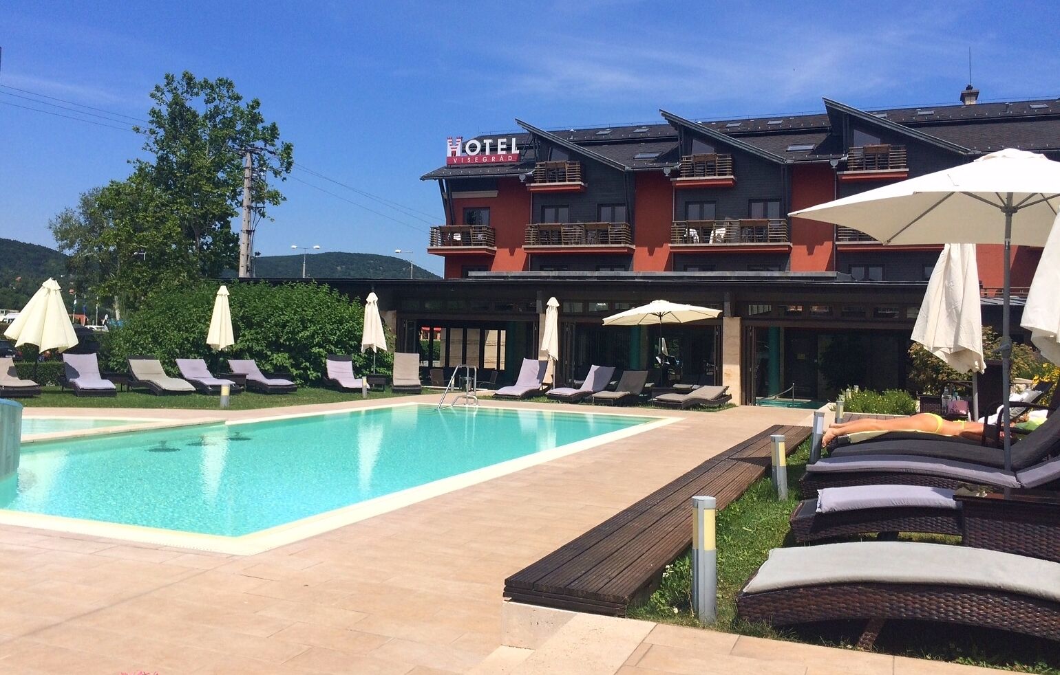 A hotel with a swimming pool, lounge chairs, and umbrellas.