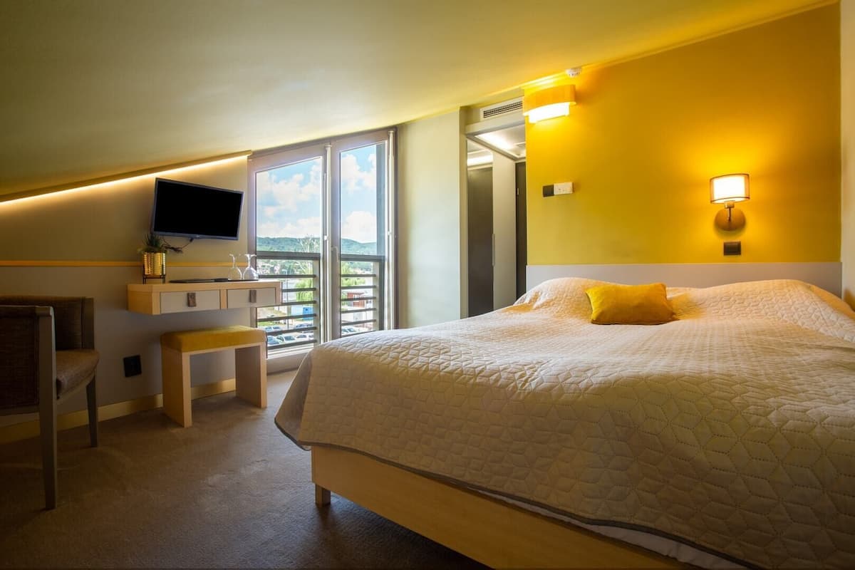 Een hotelkamer met een bed, een bureau, een stoel, een televisie en een balkon met uitzicht.