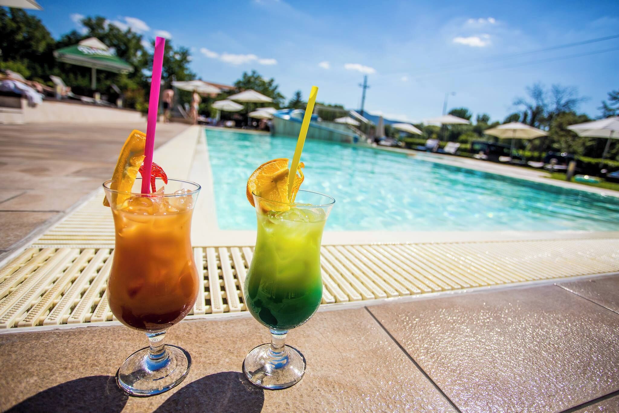 Two drinks with straws and fruit slices on a poolside deck.