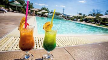 Two drinks with straws and fruit slices on a poolside deck.