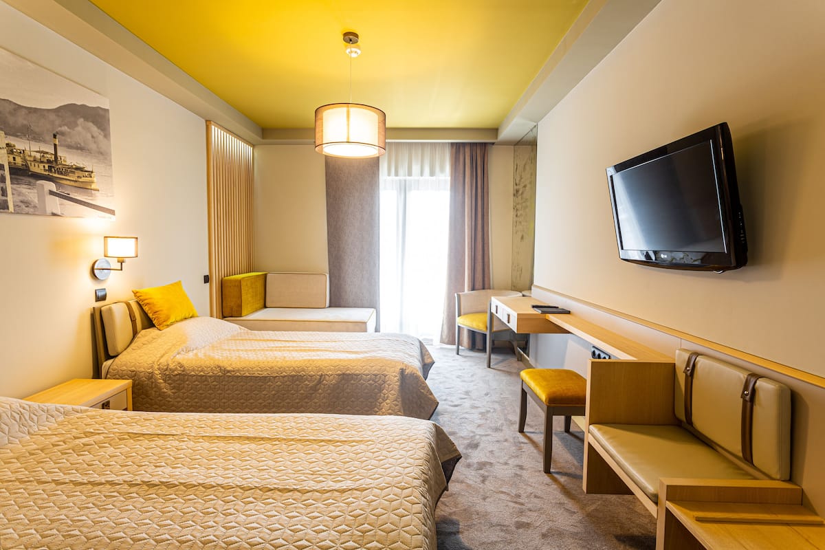 Hotelkamer met twee bedden, een bureau, een stoel, een televisie en een raam met gordijnen.
