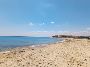 A sandy beach with a clear blue sky and calm sea.