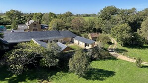 Propiedad rural con varias construcciones, incluyendo una casa principal con techo inclinado y una estructura más pequeña con techo plano. Un sendero de tierra conduce a la casa principal, rodeada de vegetación exuberante y árboles.