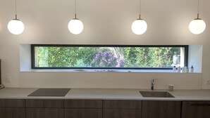 Una cocina moderna con un ventanal grande, tres lámparas colgantes y un armario de madera.