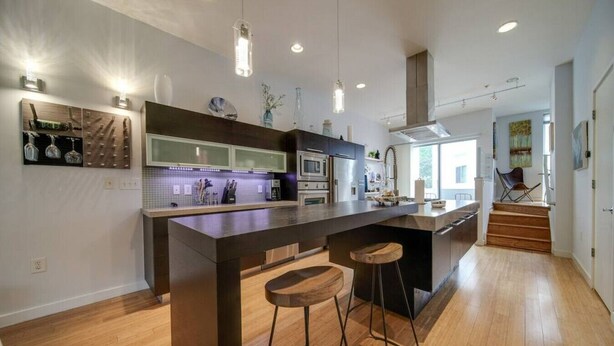 Una cocina moderna con una isla central, taburetes de bar, electrodomésticos de acero inoxidable e iluminación colgante.