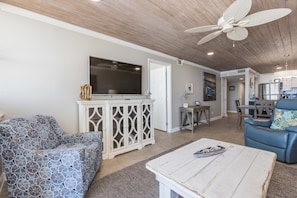 Un salon avec un meuble blanc, un canapé bleu à motifs, une table basse blanche et un ventilateur de plafond.
