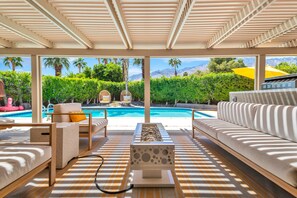 Uma área à beira da piscina com um sofá, uma cadeira e uma mesa.