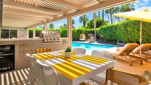 Un patio exterior con una parrilla, piscina y sillones de descanso.