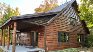 A rustic cabin with a stone foundation, wooden deck, and a chimney. - Short Drive to Trails, Secluded in the Hiawatha National Forest (Wetmore)