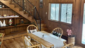 A wooden cabin interior with a dining area, staircase, and large windows. - Short Drive to Trails, Secluded in the Hiawatha National Forest (Wetmore)