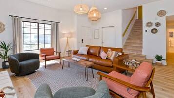 A spacious living room with a large window, a sofa set, a coffee table, and a staircase leading to another level.