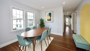 A dining area with a wooden table and teal chairs, a potted plant, and a framed abstract artwork on the wall. - Luke 2 House, Stylish, Boston, Parking, Sleeps 8, Memorable  (Everett)