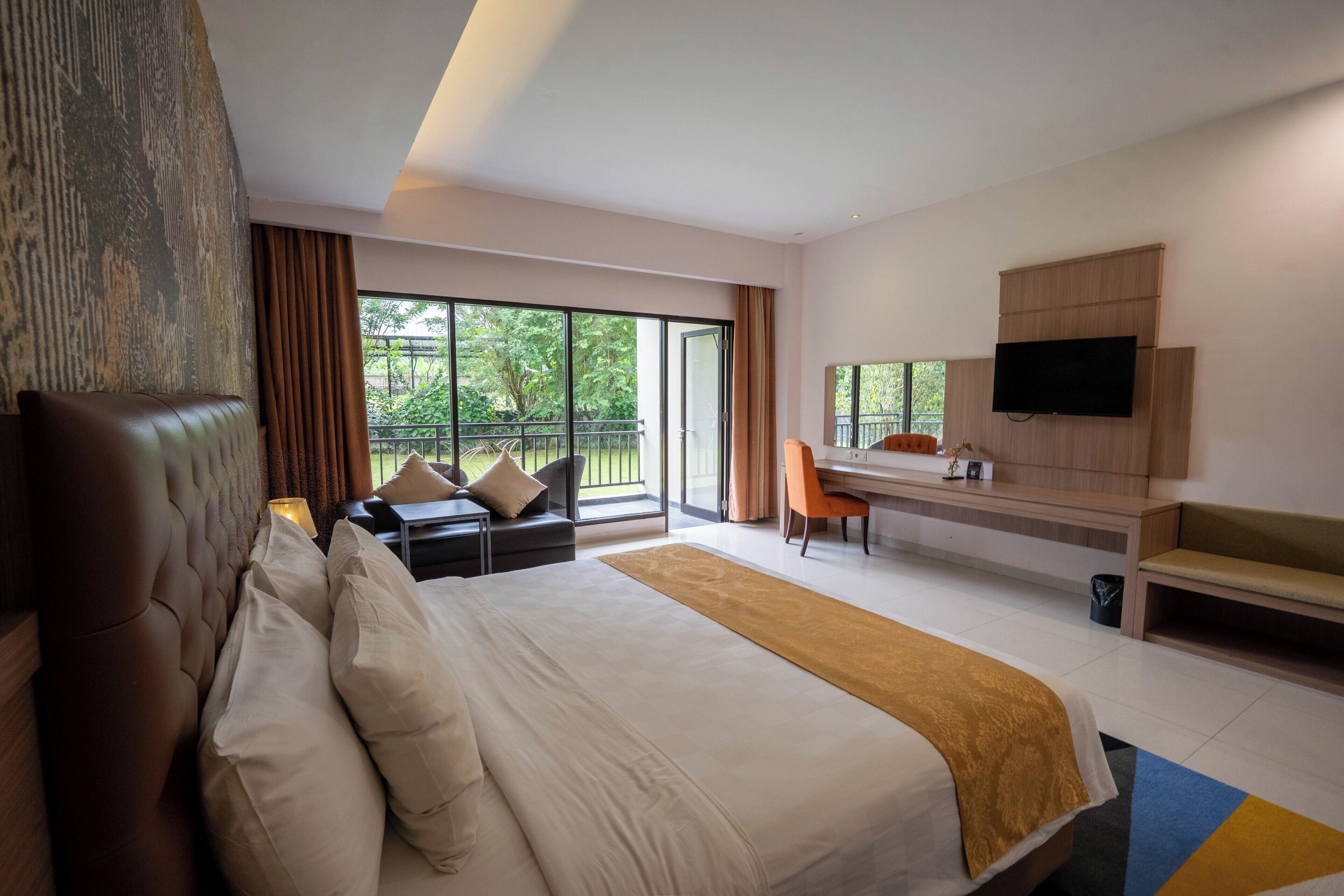 Une chambre d’hôtel moderne dotée d ’un grand lit, d’un bureau, d’une télévision et d’un balcon offrant une vue sur la verdure.