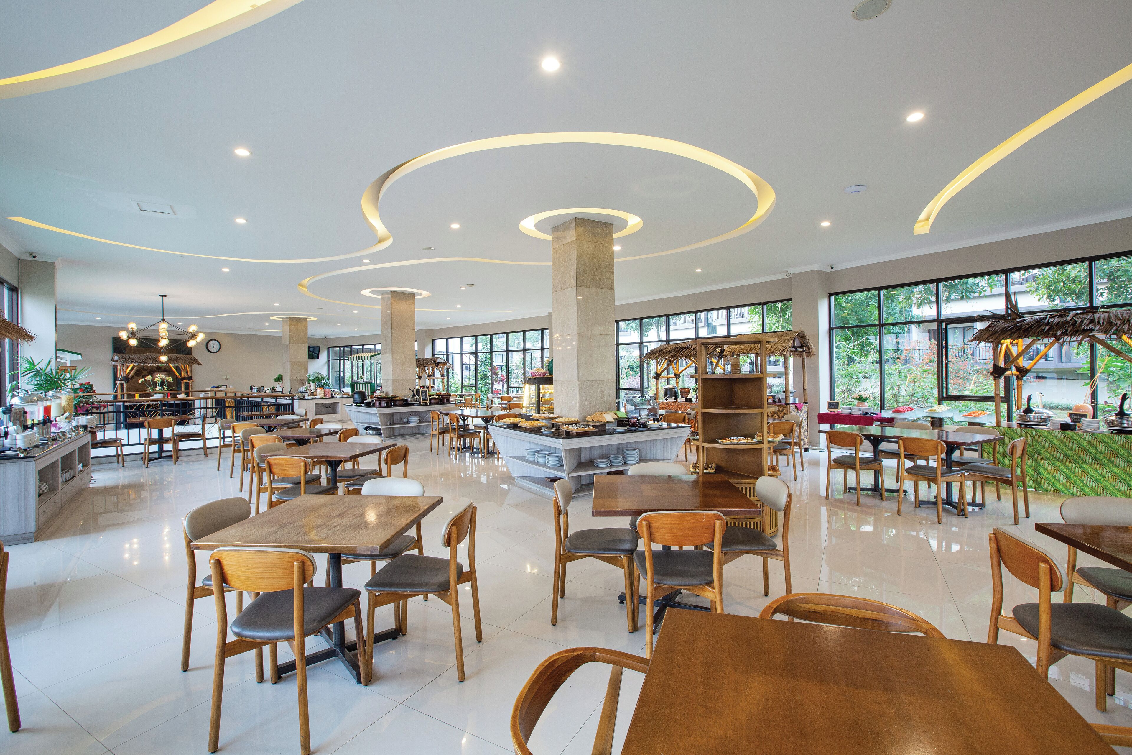 A spacious cafe with wooden tables and chairs, a central island with seating, and large windows offering a view of the outdoors.