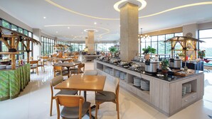 A spacious hotel dining area with a central island, multiple seating arrangements, and large windows offering views. - The Green Peak, ARTOTEL Curated (Megamendung)