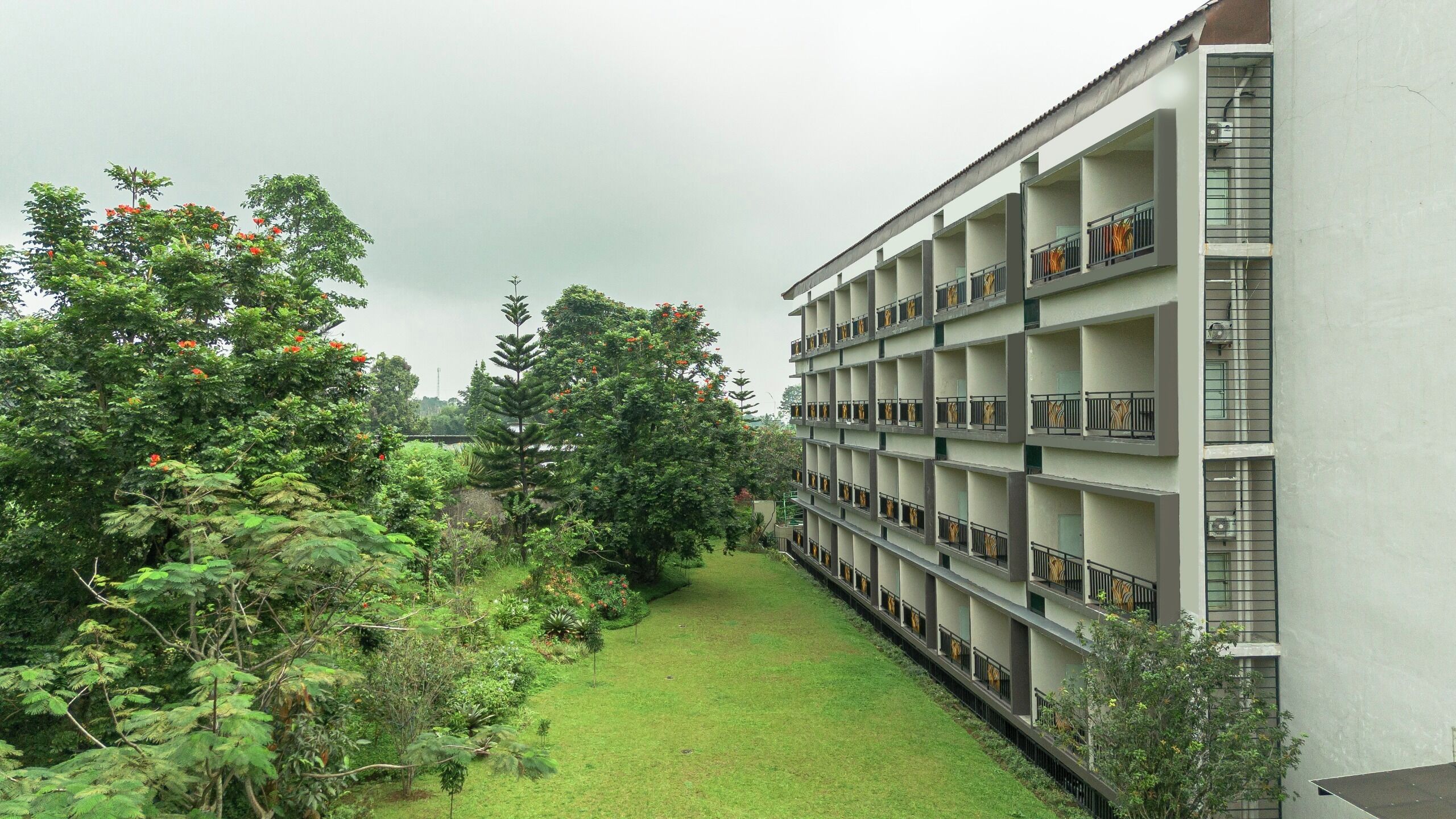 A multi-story building with balconies, surrounded by lush greenery and a well-maintained lawn.