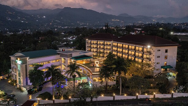 A hotel with multiple floors, a courtyard with a heart-shaped light, and a view of surrounding mountains. - The Green Peak, ARTOTEL Curated (Megamendung)
