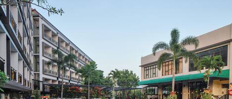 A swimming pool with lounge chairs and a covered seating area, surrounded by buildings with balconies and palm trees.