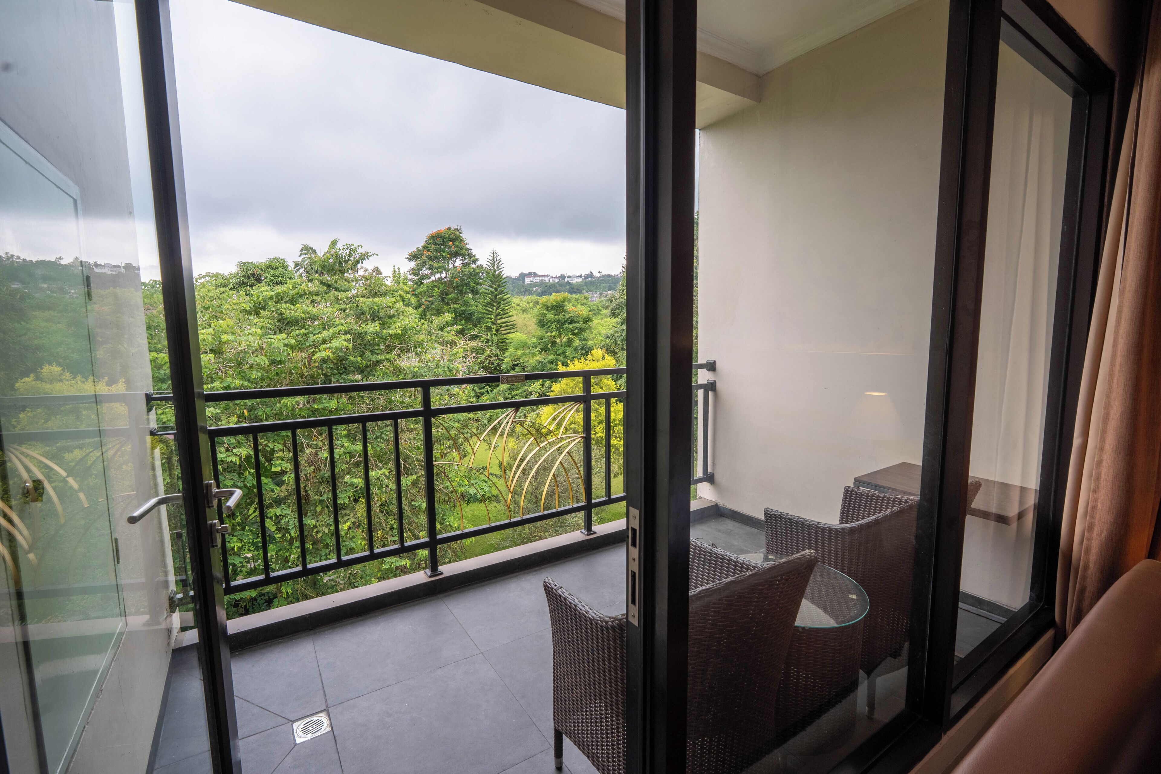 A balcony with wicker furniture, a glass door, and a view of greenery.