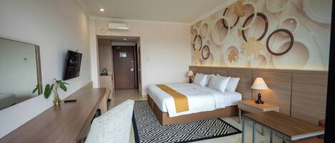 A hotel room with a bed, bedside table, lamp, desk, chair, TV, and a decorative wall.