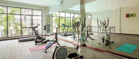 A gym with cardio machines, mirrors, and exercise mats.