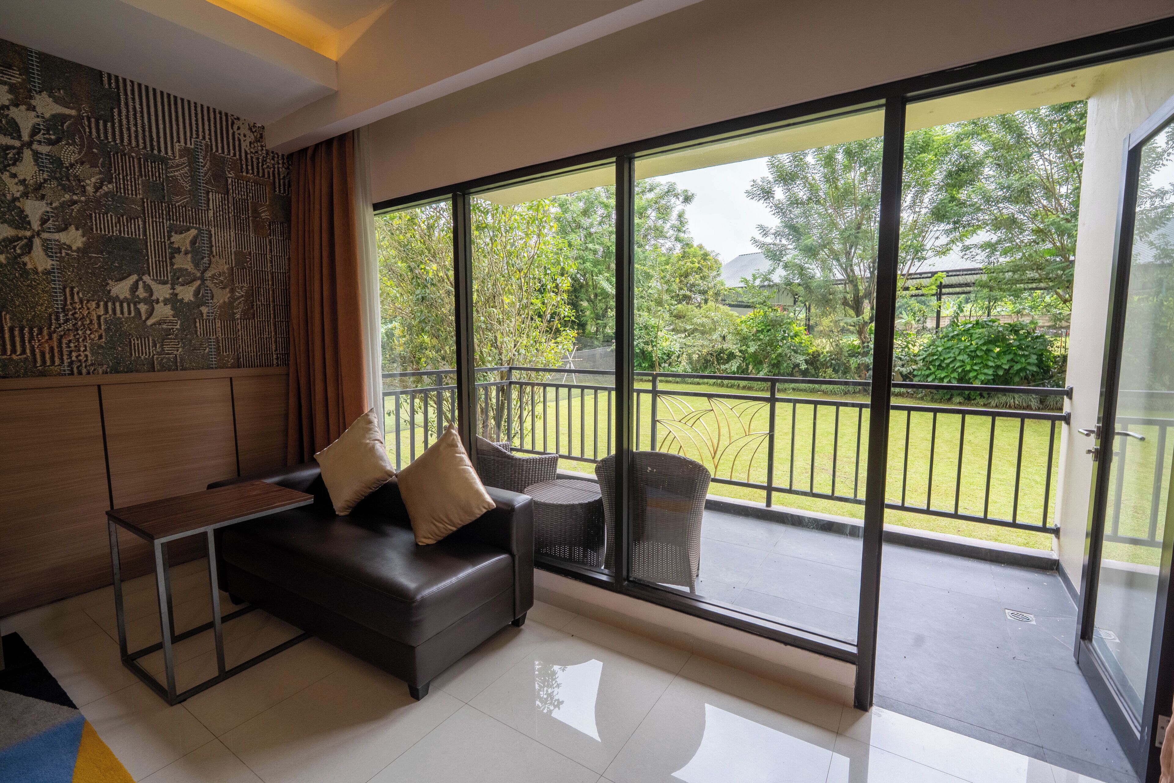 A modern living room with a sofa, a small table, and a balcony with a view of greenery.